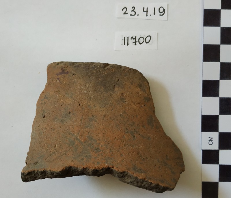 Фрагмент стінки ліпного сіроглиняного посуду червонуватого кольору зовні.