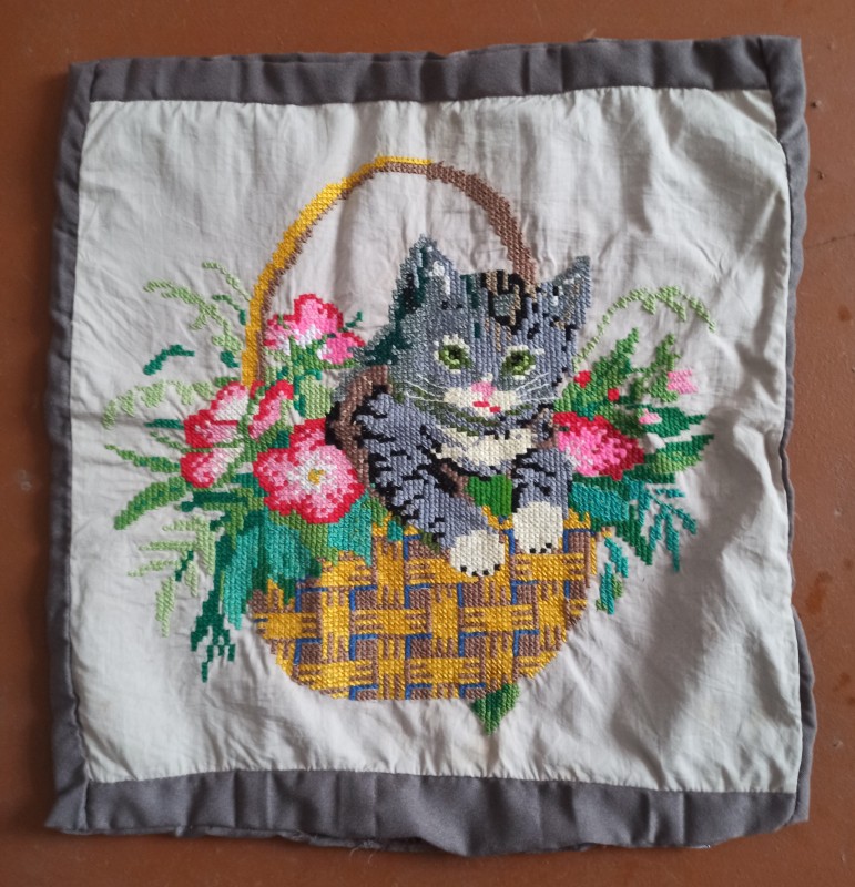 Наволочка з вишитим квітковим орнаментом та кішкою, яка сидить у кошику.